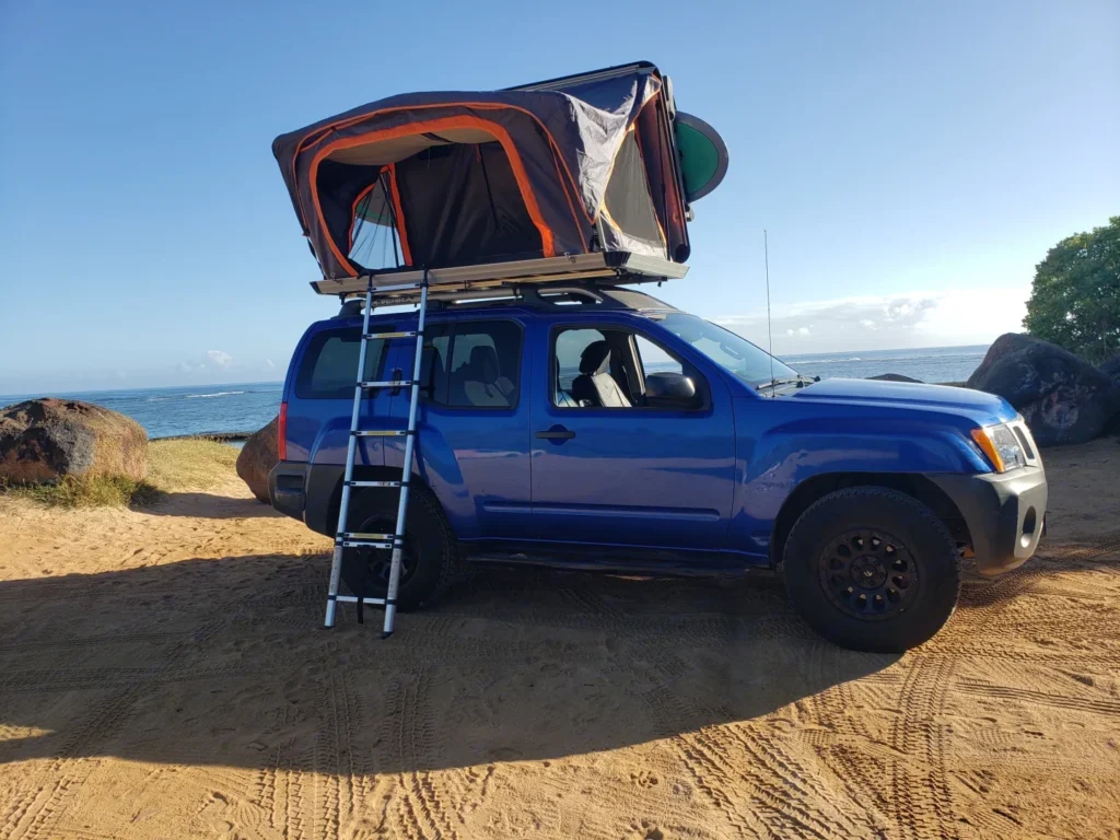 Blue Xterra 4x4 camper in Makawao, Hawaii, with a premium hardtop rooftop tent and camping gear included. This 15-foot camper sleeps up to 4 guests with a full-size bed, accommodates up to 5 passengers, has a 4.7-star rating from 199 trips, offers delivery within 15 miles, includes unlimited mileage, and is not pet-friendly.