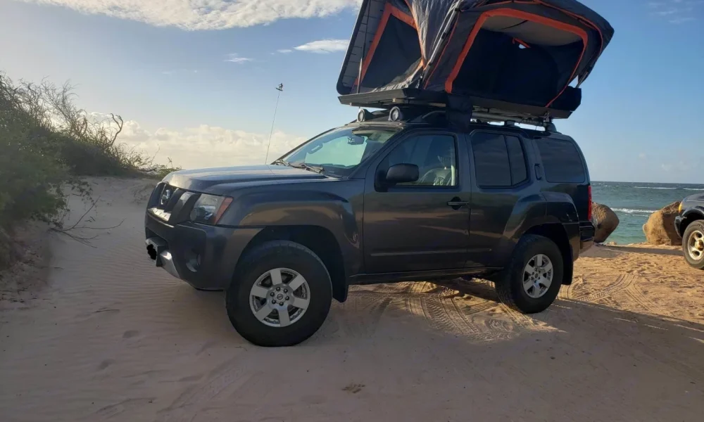 Gunmetal Xterra 4x4 truck camper in Makawao, Hawaii, with a premium rooftop tent. This 14-foot camper sleeps up to 4 guests with a full-size bed, accommodates up to 5 passengers, has a 4.7-star rating from 66 trips, offers delivery within 15 miles, includes unlimited mileage, and is not pet-friendly.