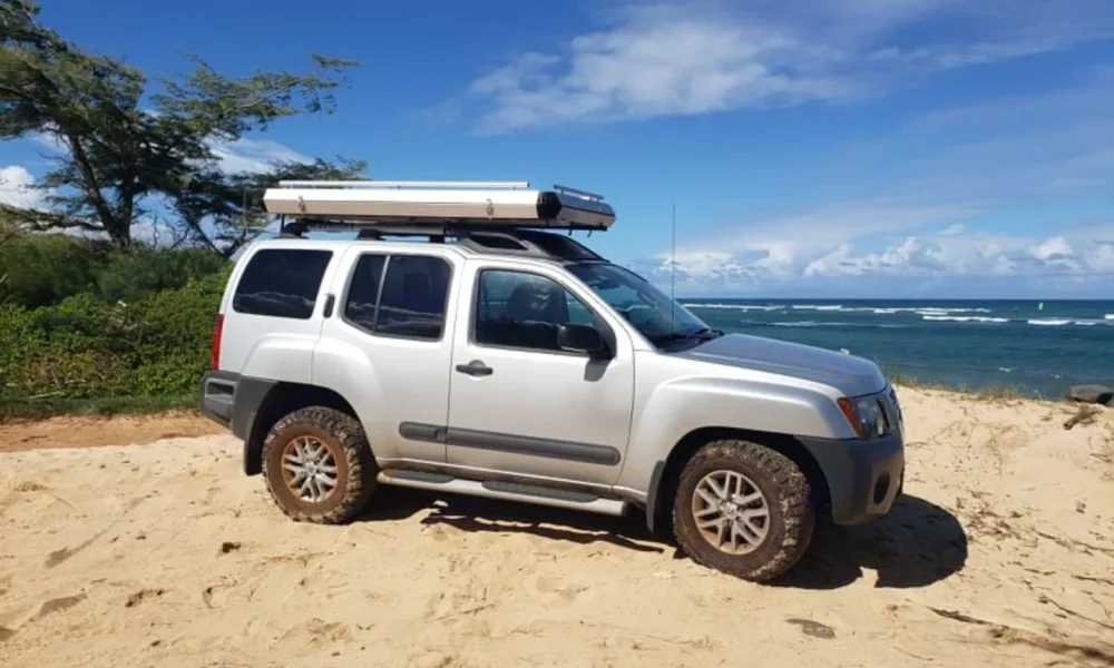 Silver Xterra 4x4 truck camper in Makawao, Hawaii, with a premium rooftop tent and camping gear included. This 14-foot camper sleeps up to 4 guests with a full-size bed, accommodates up to 5 passengers, has a 4.9-star rating from 123 trips, offers delivery within 15 miles, includes unlimited mileage, and is not pet-friendly.